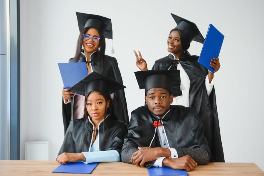 education, graduation and people concept - group of happy international graduate students in mortar boards and bachelor gowns with diplomas